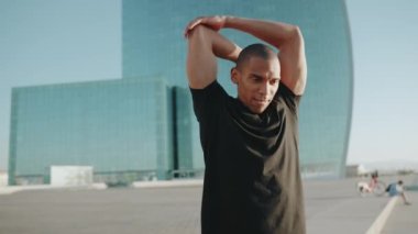 Siyah tişört giyen güçlü kel sporcu sabahları dışarıda egzersiz yapıyor.