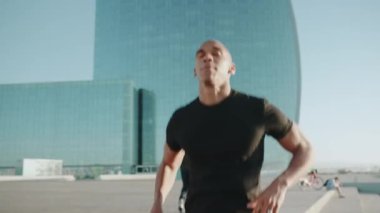 Siyah tişört giyen güçlü kel sporcu sabahları açık havada sıçrıyor.