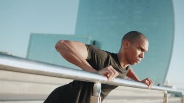 Siyah tişört giyen konsantre kel sporcu sabahları korkuluklardan şınav çeker.