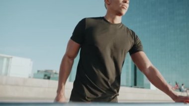 Siyah tişört giyen kel bir sporcu sabahları dışarı bakıyor.