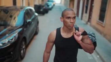 Siyah tişört giyen kel, ciddi bir sporcu şehirde yürüyor.