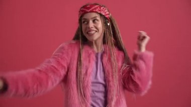 Gülen hippi kadın pembe stüdyoda kameraya poz veriyor.