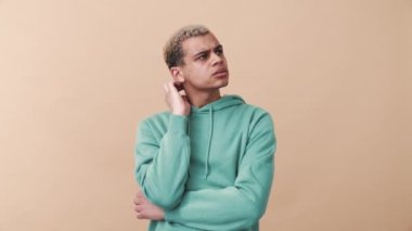 Mavi kapüşonlu, kıvırcık saçlı adamın bej rengi stüdyoda bir fikri var.