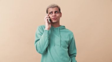 Mavi kapüşonlu yakışıklı adam bej stüdyoda telefonla konuşuyor.