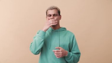 Hoşnut olmayan kıvırcık saçlı mavi kapüşonlu adam bej stüdyoda kötü kokudan muzdarip.