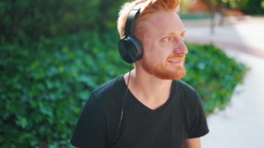 Pozitif kızıl saçlı adam bankta otururken kulaklıkla müzik dinliyor.