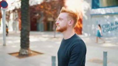 Düşünceli kızıl saçlı adam dışarıda yürüyor.