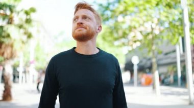 Endişeli kızıl saçlı adam dışarıda dolaşıyor ve etrafa bakıyor.