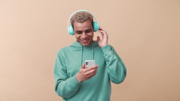 Veselý Kudrnatý Muž Modré Mikině Poslouchající Hudbu Sluchátkách Béžovém Studiu — Stock video