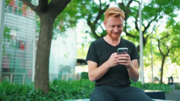 Sorrindo Homem Ruivo Mensagens Texto Por Smartphone Enquanto Sentado Banco — Vídeo de Stock
