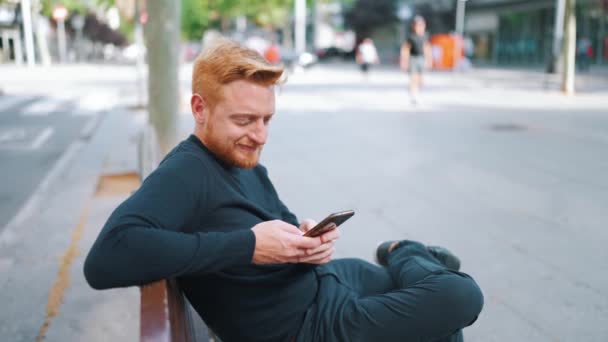 Relaxado Gengibre Homem Mensagens Texto Por Smartphone Enquanto Sentado Banco — Vídeo de Stock