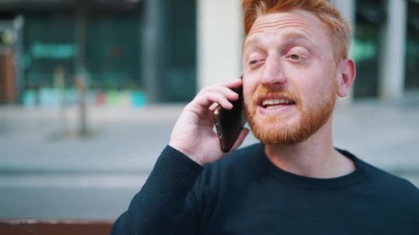 Homem Gengibre Positivo Falando Por Smartphone Enquanto Sentado Banco Livre — Vídeo de Stock