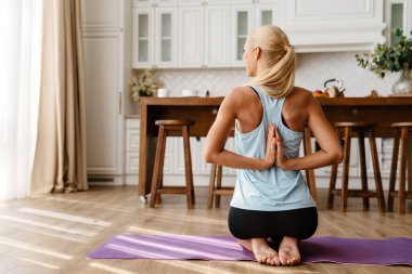 Evde yoga yaparken egzersiz yapan sarışın genç bir kadın.