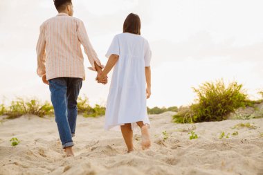 Yaz plajında yürürken el ele tutuşan çok ırklı bir çift.