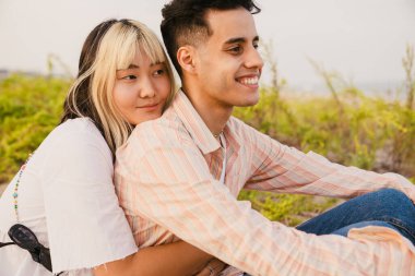 Yaz kumsalında dinlenirken gülümseyen ve sarılan çok ırklı bir çift.