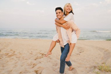 Yaz plajında sırtına binerken gülümseyen çok ırklı genç bir çift.