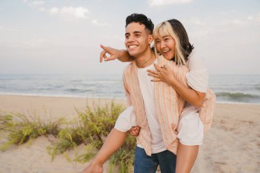 Yaz plajında sırtına binerken gülümseyen çok ırklı genç bir çift.