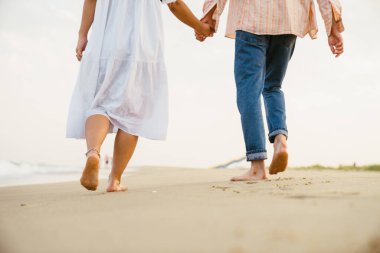 Yaz plajında yürürken el ele tutuşan çok ırklı bir çift.