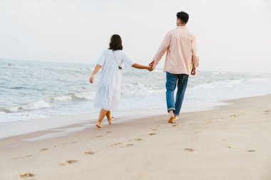 Yaz plajında yürürken el ele tutuşan çok ırklı bir çift.