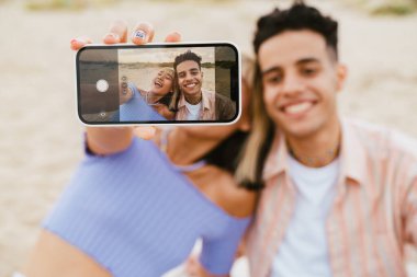 Genç, çok ırklı bir çift yaz plajında cep telefonuyla selfie çekiyor.