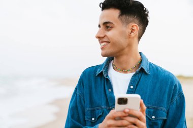Yaz plajında cep telefonu kullanırken gülümseyen genç bir ortadoğulu.