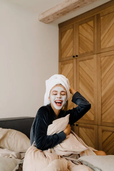 Mujer Joven Con Máscara Facial Riendo Mientras Sienta Cama Casa — Foto de Stock