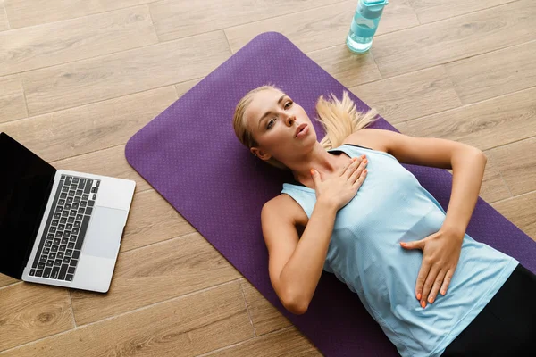 Blonde young woman doing breathing exercise during yoga practice at home