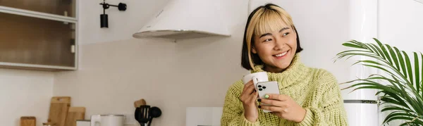 Asiatisk Jente Smiler Bruker Mobiltelefon Mens Hun Drikker Hjemme – stockfoto