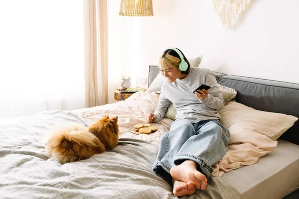 Gadis Asia Dengan Headphone Menggunakan Ponsel Saat Beristirahat Dengan Anjingnya — Stok Foto