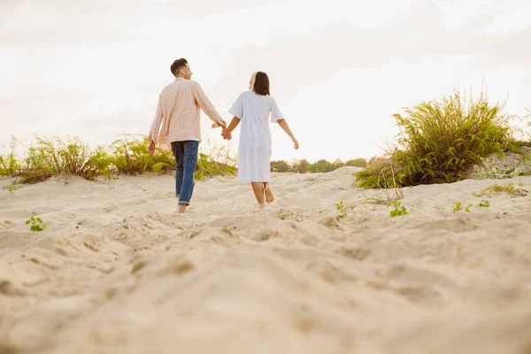 Yaz plajında yürürken el ele tutuşan çok ırklı bir çift.