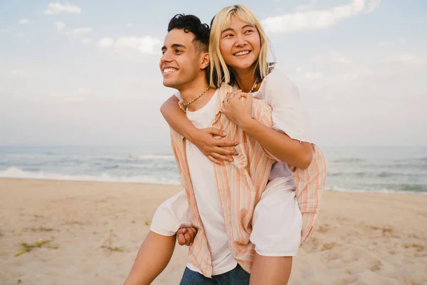 多人種の若いカップルが笑顔で夏のビーチでピギーバック — ストック写真