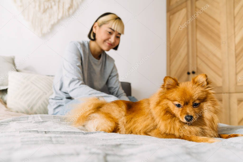Asian girl smiling while resting with her dog on bed at home