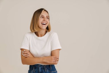 Kollarını kavuşturup gülümseyen genç sarışın kadın beyaz arka planda izole edilmiş.