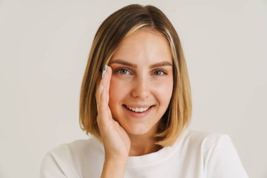 Beyaz arka planda izole edilmiş kameraya bakarken gülümseyen genç sarışın kadın.