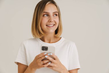 Beyaz arka planda izole edilmiş cep telefonu kullanırken gülümseyen genç sarışın kadın.