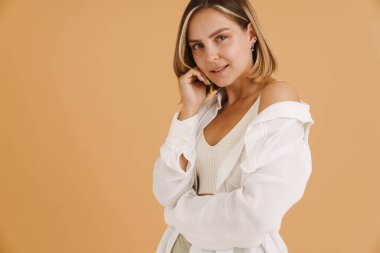 Gömlek giyen genç sarışın kadın poz veriyor ve bej arka planda izole edilmiş kameraya bakıyor.