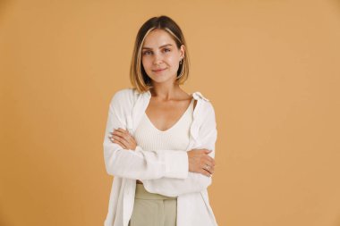 Bej arka planda izole edilmiş kameraya bakarken gülümseyen genç sarışın kadın.