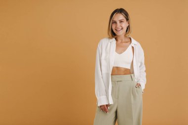 Bej arka planda izole edilmiş kameraya bakarken gülümseyen genç sarışın kadın.