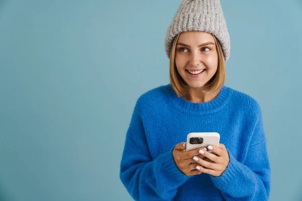 Молода Блондинка Трикотажному Капелюсі Посміхається Використовує Мобільний Телефон Ізольовано Синьому — стокове фото