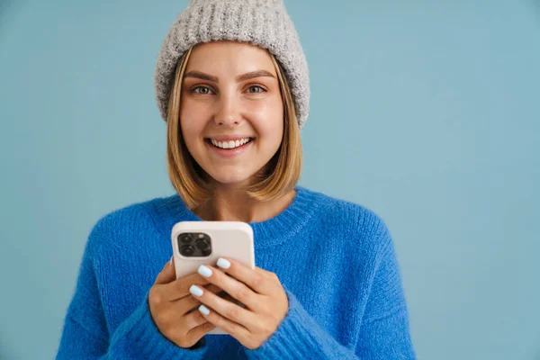 Молода Блондинка Трикотажному Капелюсі Посміхається Використовує Мобільний Телефон Ізольовано Синьому — стокове фото