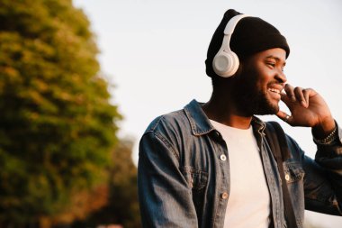 Siyah genç adam parkta yürürken kulaklıkla müzik dinliyor.