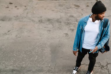 Kulaklıklı siyahi bir adam dışarıda beklerken cep telefonu kullanıyor.