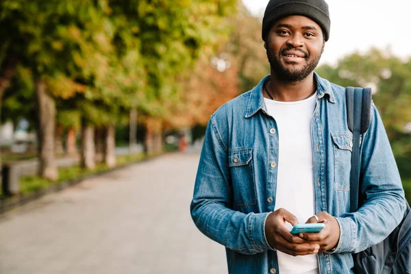 夏の公園を歩きながら携帯電話を使う黒人青年 — ストック写真