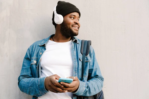 ヘッドフォンの笑顔と屋外で携帯電話を使用して黒の若い男 — ストック写真