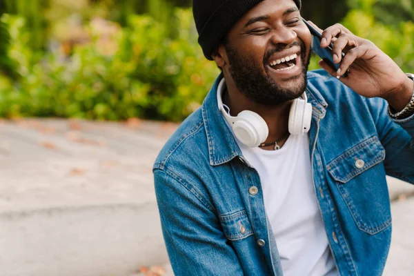 秋の公園を歩きながら携帯電話で話してヘッドフォンを持つ黒人男性 — ストック写真