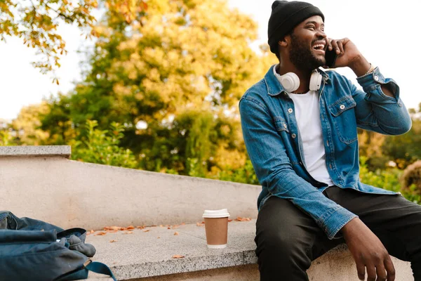 秋の公園で休んでいる間に携帯電話で話してヘッドフォンを持つ黒人男性 — ストック写真
