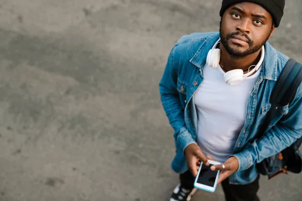 Hombre Negro Con Auriculares Usando Teléfono Móvil Mientras Está Parado —  Fotos de Stock