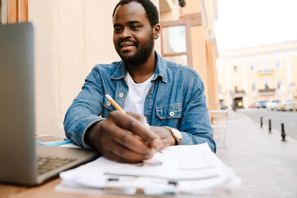Μαύρος Νεαρός Που Εργάζεται Laptop Και Χαρτιά Ενώ Κάθεται Cafe — Φωτογραφία Αρχείου