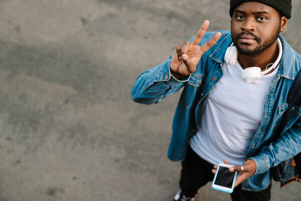 Black Young Man Headphones Gesturing Using Mobile Phone Outdoors Stock Photo