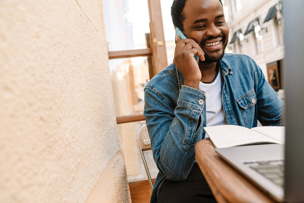 Black Man Talking Cellphone While Working Laptop Cafe Outdoors Stock Picture